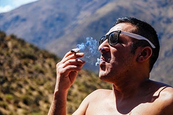 Young man smoking cannabis, man with sunglasses and mountains background