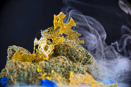 Macro detail of cannabis nugs and marijuana concentrates (aka shatter) with smoke isolated over black