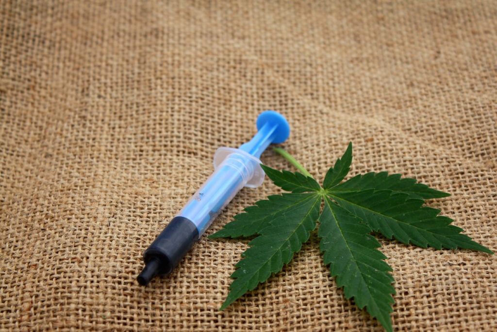 syringe with rso oil next to a cannabis leaf