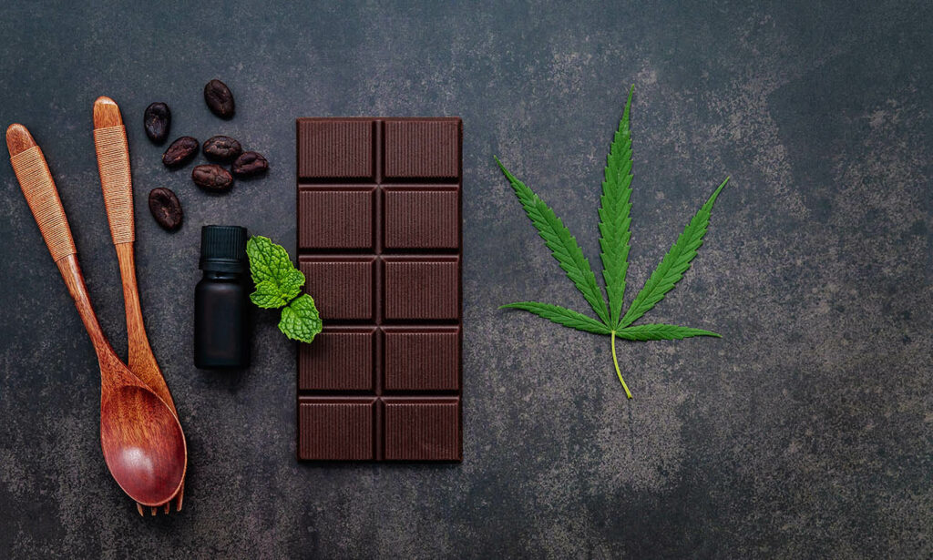Food conceptual image of cannabis leaf with dark chocolate and fork on dark concrete background.